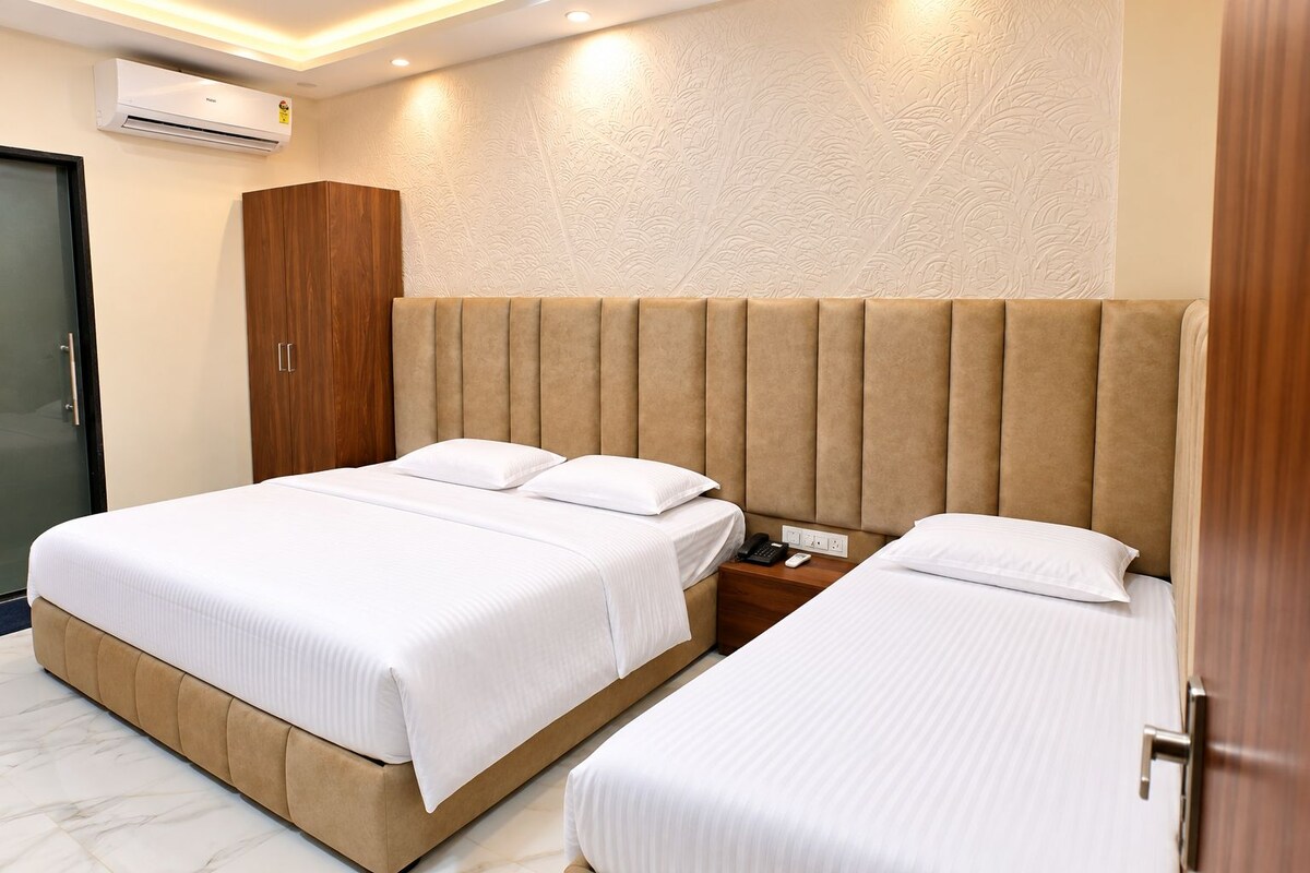 A hotel room with two beds, a wooden wardrobe, a bedside table with a phone, and an air conditioning unit.