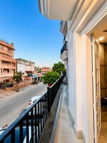Un balcon donnant sur une rue, un pot de fleurs et un bâtiment avec une enseigne.