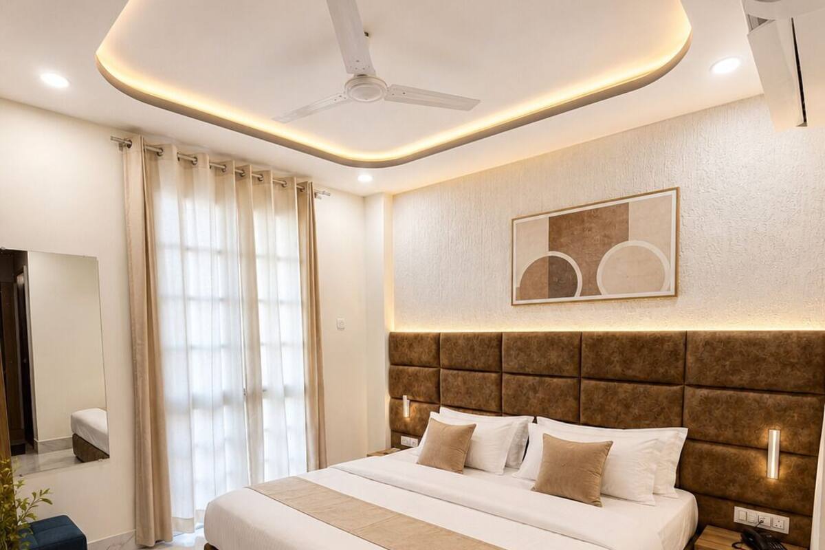 Una habitación de hotel moderna con una cama grande, un ventilador de techo, una mesita de noche con un teléfono y un ventanal con cortinas.