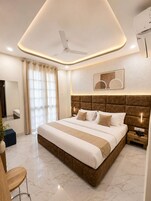 Une chambre d’hôtel moderne dotée d’un grand lit, d’un ventilateur de plafond, d’une table de chevet avec un téléphone et d’une grande fenêtre avec des rideaux.