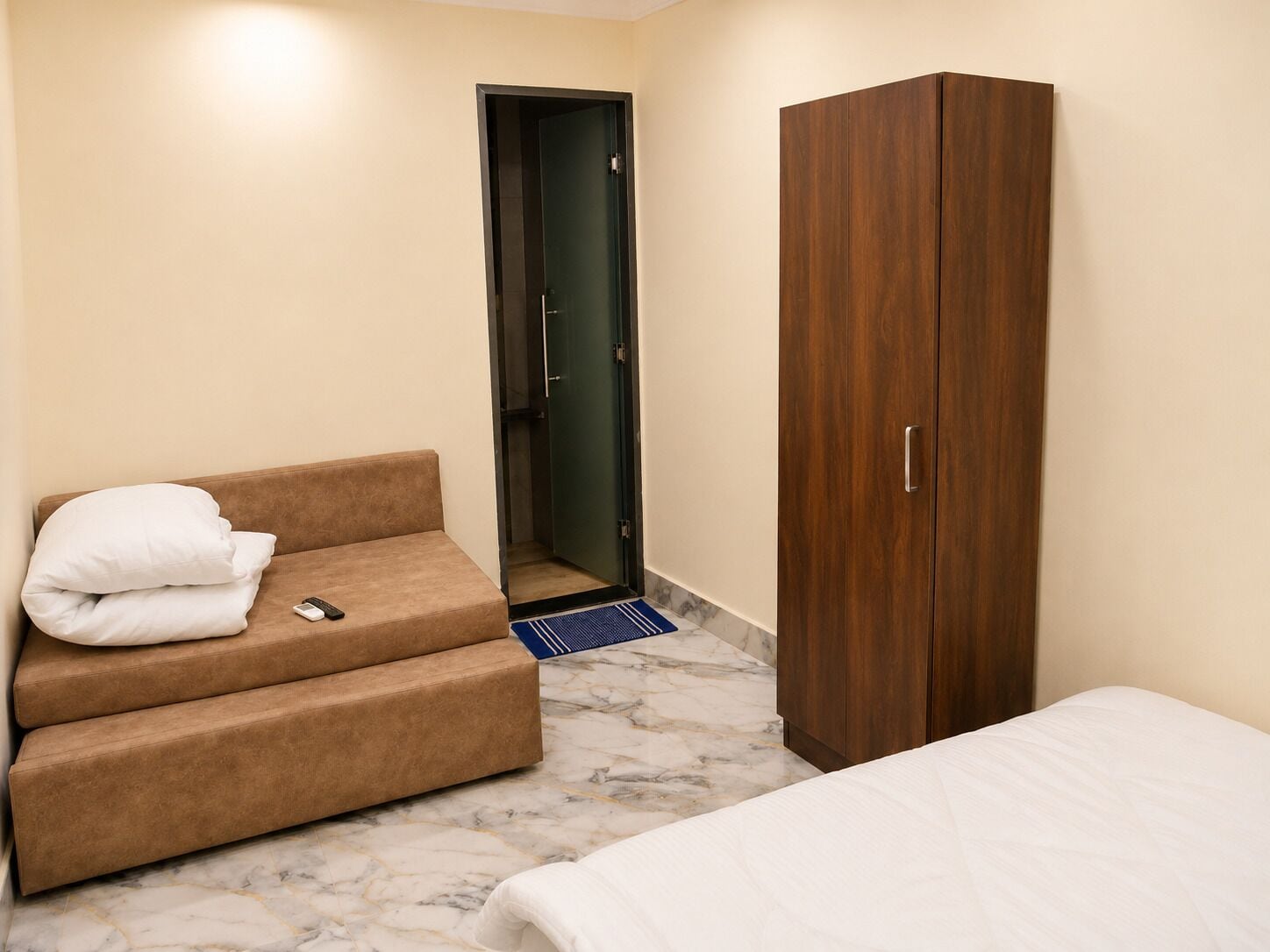 A room with a sofa, a wardrobe, a bed, and a door leading to a bathroom.