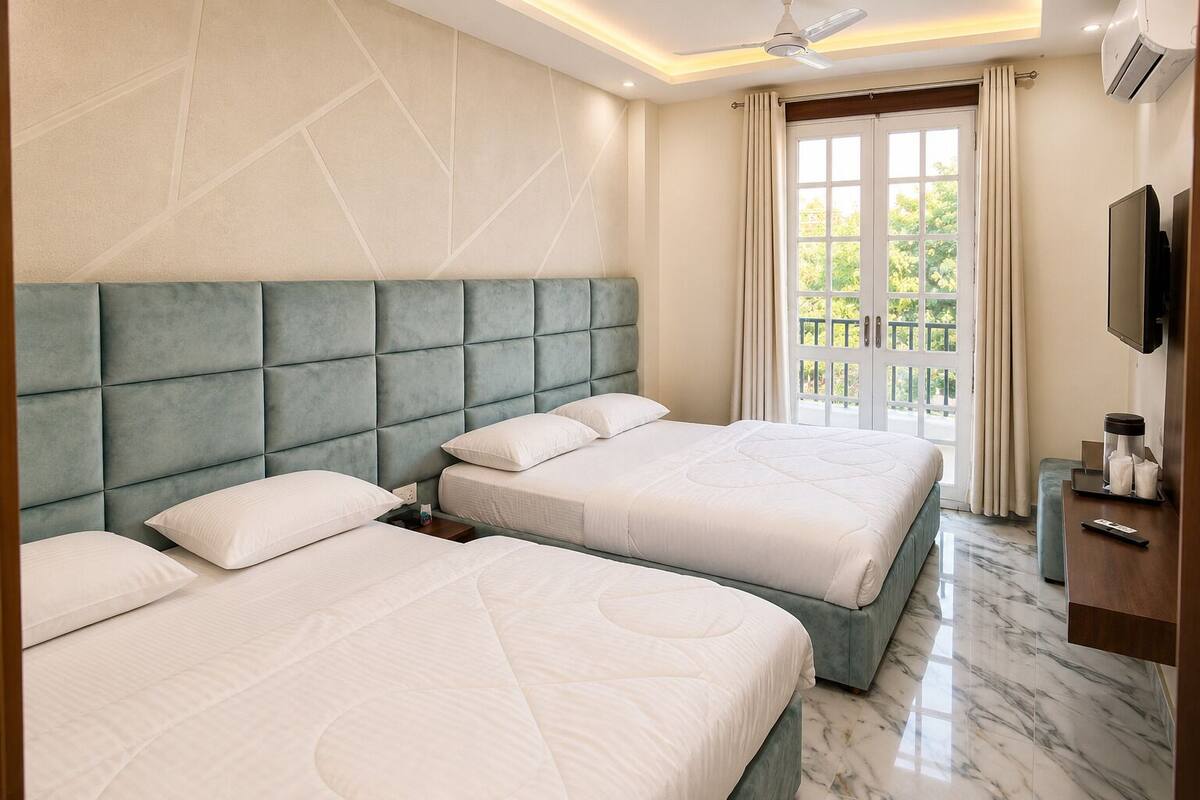 Habitación de hotel con dos camas, un televisor y un balcón con cortinas.