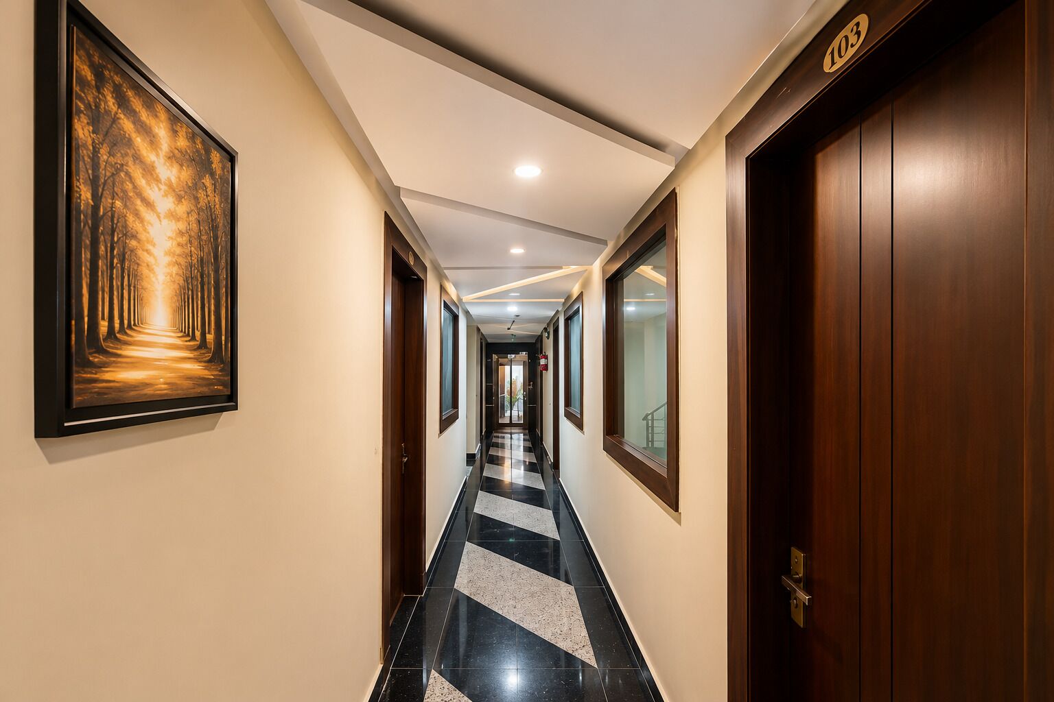 A hotel hallway with a framed forest painting, a checkered floor, and a door with the number 103.