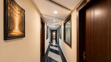 A hotel hallway with a framed forest painting, a checkered floor, and a door with the number 103.