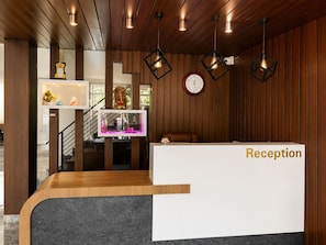 Ett välkomstområde med en receptionsdisk i trä, en klocka och hängande lampor.