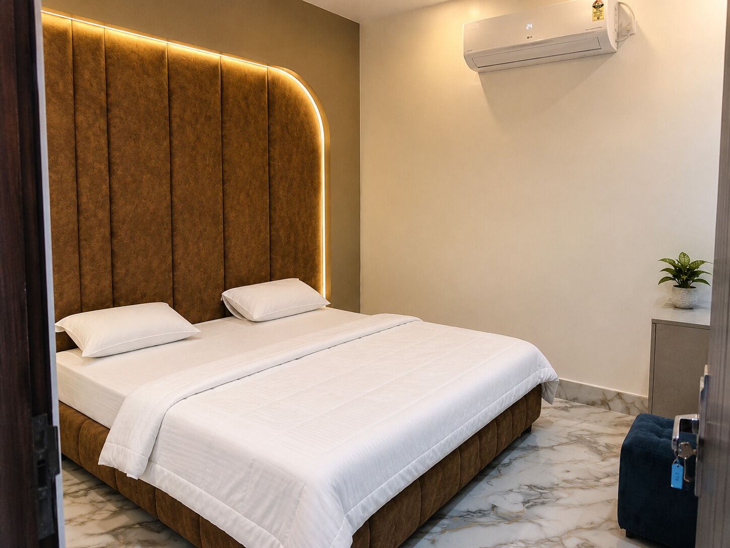 Une chambre d’hôtel avec un lit, un climatiseur fixé au mur, une petite plante en pot et un sol en marbre.