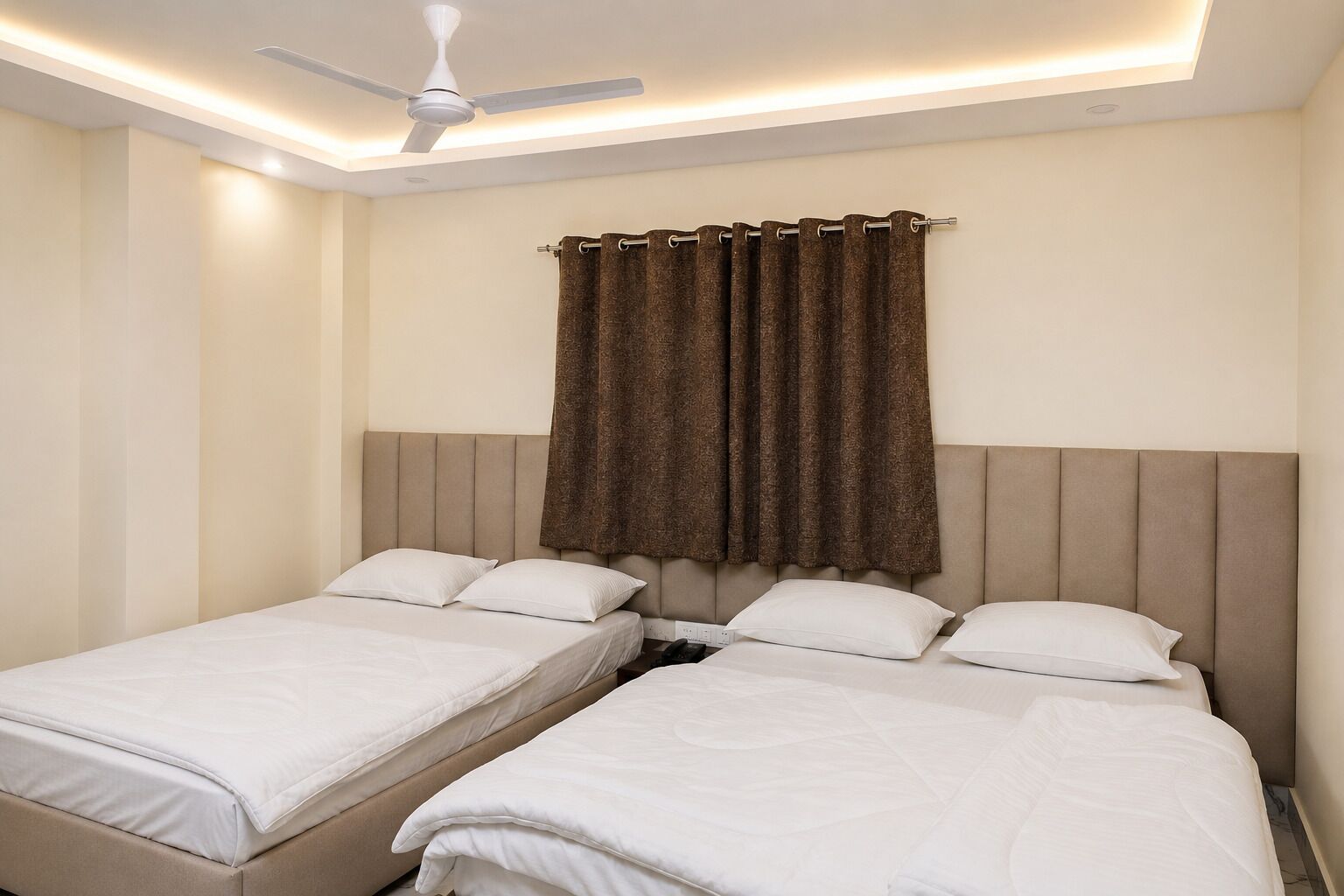 A hotel room with two single beds, a ceiling fan, and a window with brown curtains.