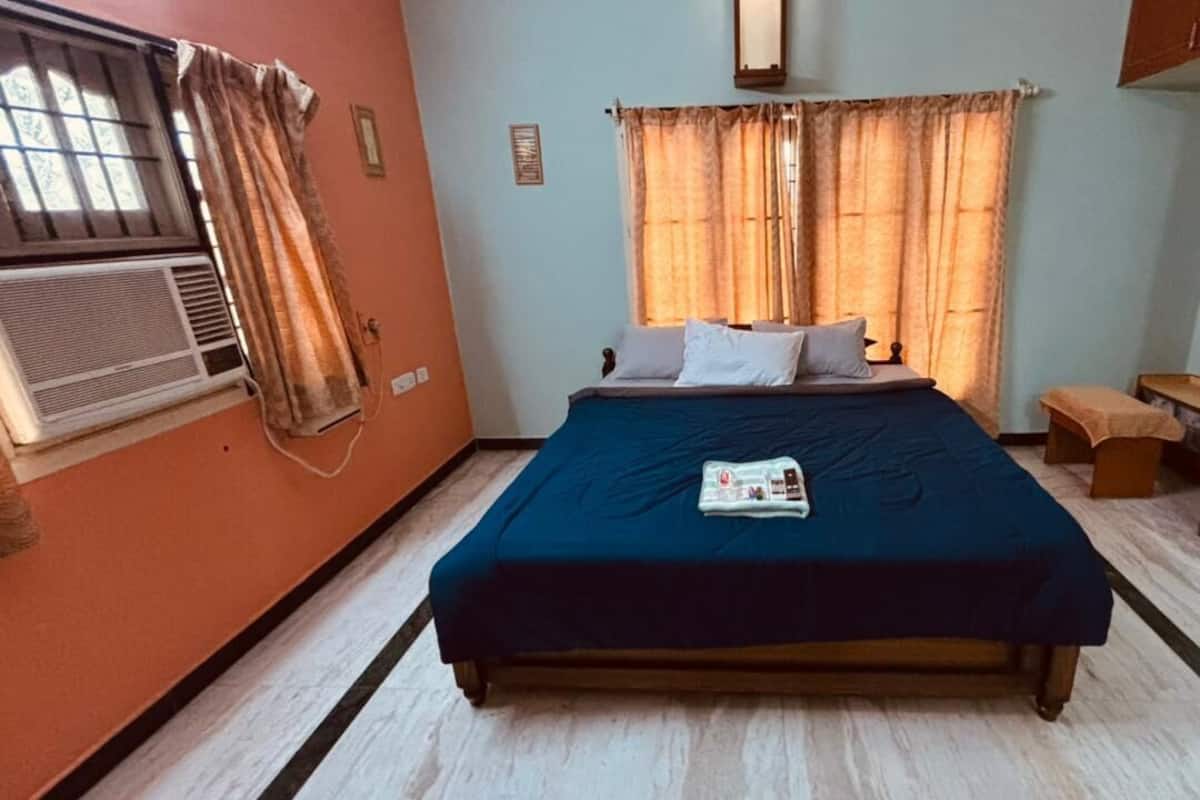 A bedroom with a bed, a window with curtains, a radiator, and a wooden bench.