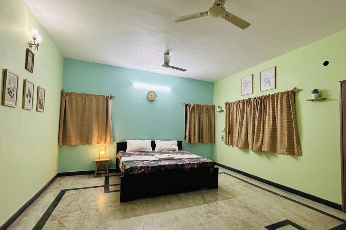 A bedroom with a bed, a ceiling fan, a wall clock, and curtains.