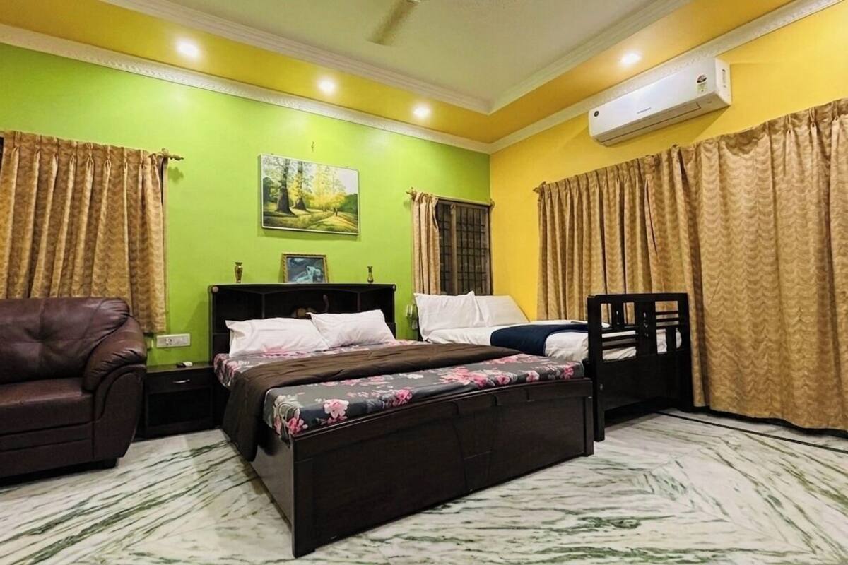 A bedroom with a bed, a chair, a nightstand, a picture on the wall, and an air conditioner.