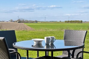 Une table ronde entourée de chaises, installée dans un champ d’herbe, avec des éoliennes en arrière-plan.