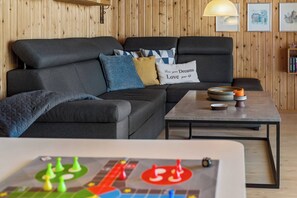 Un salon moderne avec un canapé d’angle, une table basse et un jeu de société au premier plan.