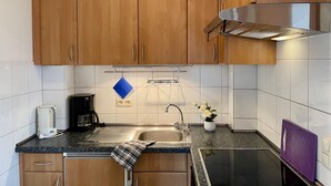 A kitchen with wooden cabinets, a stainless steel range hood, a sink, a coffee maker, and a small potted plant. - Ferienwohnung in Orth auf Fehmarn (Fehmarn)