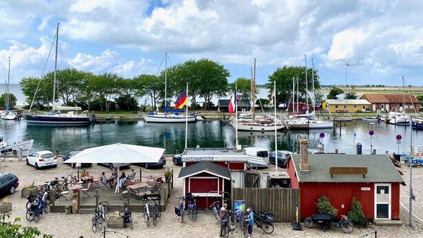 A marina with boats, a café, and a red building with a sign. - Ferienwohnung in Orth auf Fehmarn (Fehmarn)