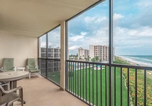 Ein Balkon mit Blick auf Strand und Meer, ein Tisch und zwei Stühle.