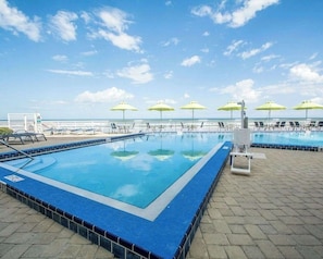 Ein Swimmingpool mit blauer Umrandung, Sonnenschirmen und Liegestühlen.