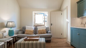 Ein gemütliches Wohnzimmer mit Sofa, einem kleinen Tisch, einer Lampe und einer Küchenzeile mit Schränken.