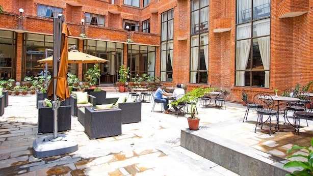 A courtyard with outdoor seating, potted plants, and a brick building with large windows. - Royal Singi Hotel (Kathmandu)