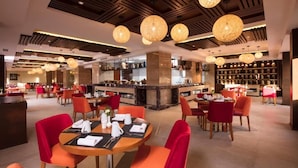 A hotel lobby with round tables, red chairs, a bar area, and a large chandelier. - Royal Singi Hotel (Kathmandu)