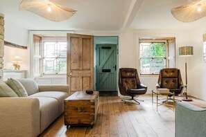 A cozy living room with a wooden chest, leather armchairs, and a green door. - Beautiful 3 Bedroom Cottage in the Cotswolds (Milton-under-Wychwood)