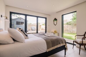 A bedroom with a large bed, a chair, and a view of the outside. - Beautiful 3 Bedroom Cottage in the Cotswolds (Milton-under-Wychwood)