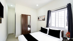 A bedroom with a bed, a wardrobe, a window with curtains, and a wall-mounted TV. - Townhouse Badangpet Crossway Hyderabad (Hyderabad)