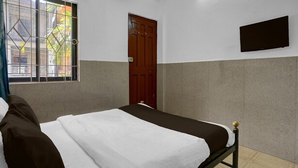 A room with a bed, a window with bars, a door, and a mounted TV. - Super Deluxe Room Hotel O Calangute Rd (Calangute)