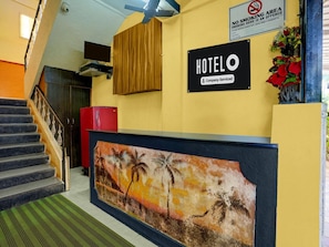 A hotel reception area with a 'HOTEL' sign, a 'NO SMOKING' sign, and a reception desk with a tropical mural.
