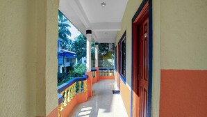 A corridor with a tiled floor, a balcony with a yellow railing, and a door with a red frame. - Super Deluxe Room Hotel O Calangute Rd (Calangute)
