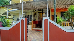 A building entrance with a red and white gate, a tiled floor, and a covered area with a metal roof. - Super Deluxe Room Hotel O Calangute Rd (Calangute)