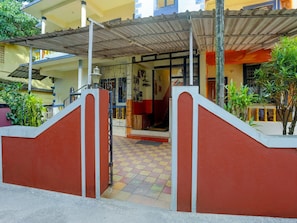 A building entrance with a red and white gate, a tiled floor, and a covered area with a metal roof.