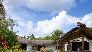 A pool with a thatched roof structure, surrounded by lush greenery and a clear sky.