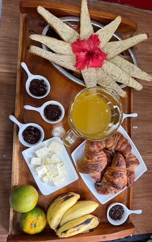 A tray with breadsticks, croissants, bananas, limes, and a mug of juice.
