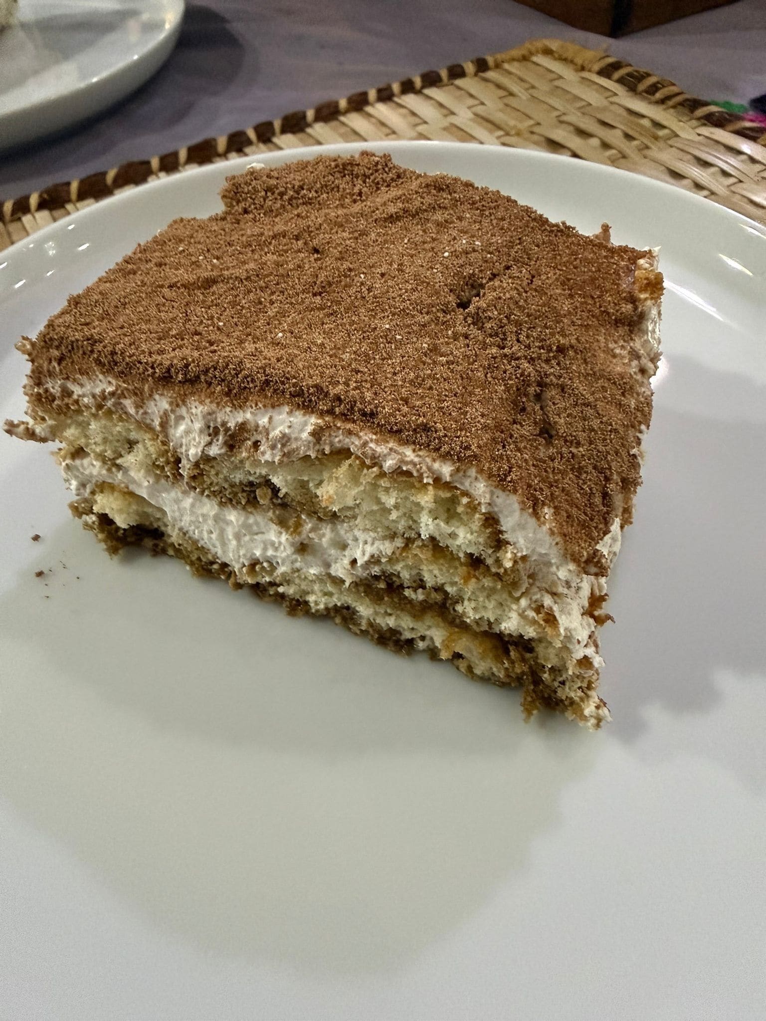 Une part de tiramisu sur une assiette blanche.