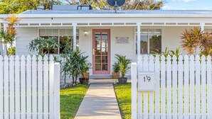 Un chalet situé en bord de mer, avec une façade blanche, une porte rouge et une plaque portant le numéro « 19 ».