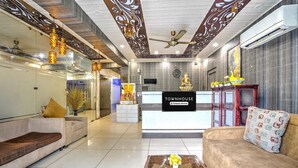 A hotel lobby with a reception desk, sofas, a coffee table, and decorative elements like a Buddha statue and a clock.