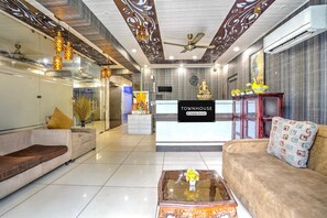 A hotel lobby with a reception desk, sofas, a coffee table, and decorative elements like a Buddha statue and a clock. - Classic With Balcony Near Medanta (Gurugram)