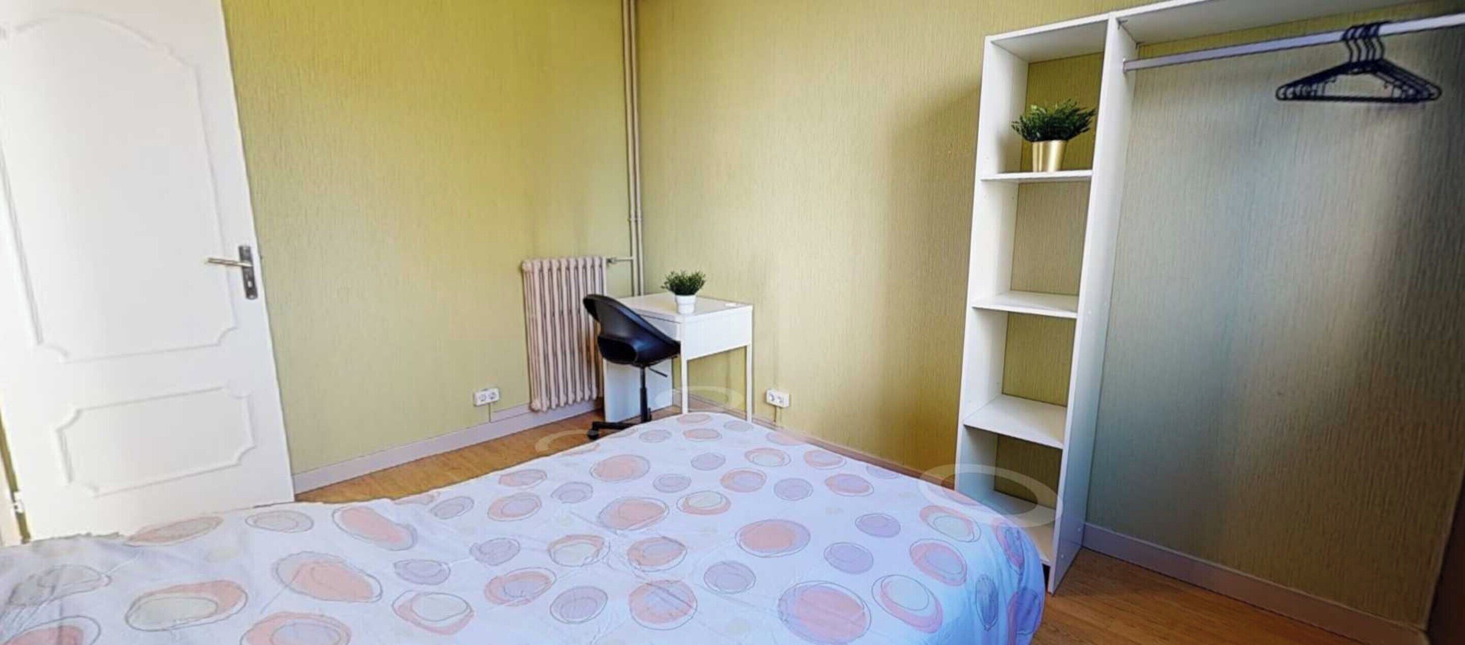A bedroom with a bed, a desk, a radiator, and a wardrobe.