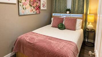 A bedroom with a bed, a ceiling fan, a nightstand, a lamp, and a window with curtains.