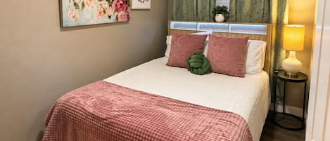 Een slaapkamer met een bed, een plafondventilator, een nachtkastje, een lamp en een raam met gordijnen.