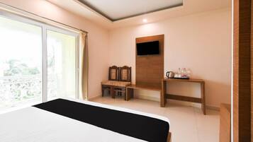 A hotel room with a bed, a TV mounted on the wall, a small table with toiletries, and a bench.
