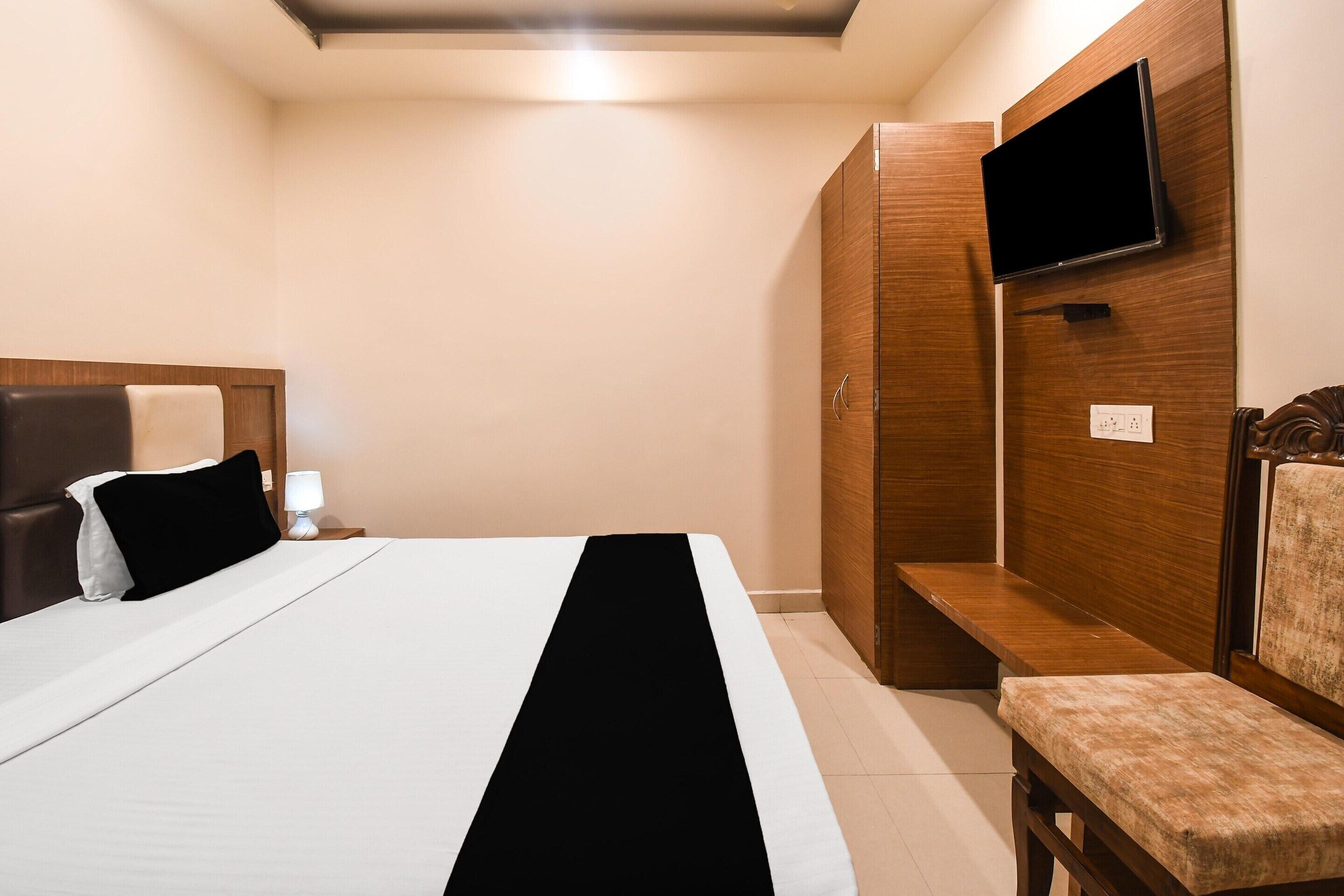 Une chambre d’hôtel comprenant un lit, un banc, un téléviseur fixé au mur et une armoire en bois.