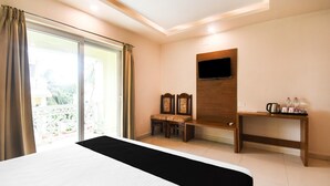 Hotelkamer met een groot bed, een aan de muur bevestigde televisie, een klein tafeltje met waterkoker en een balkon met gordijnen.