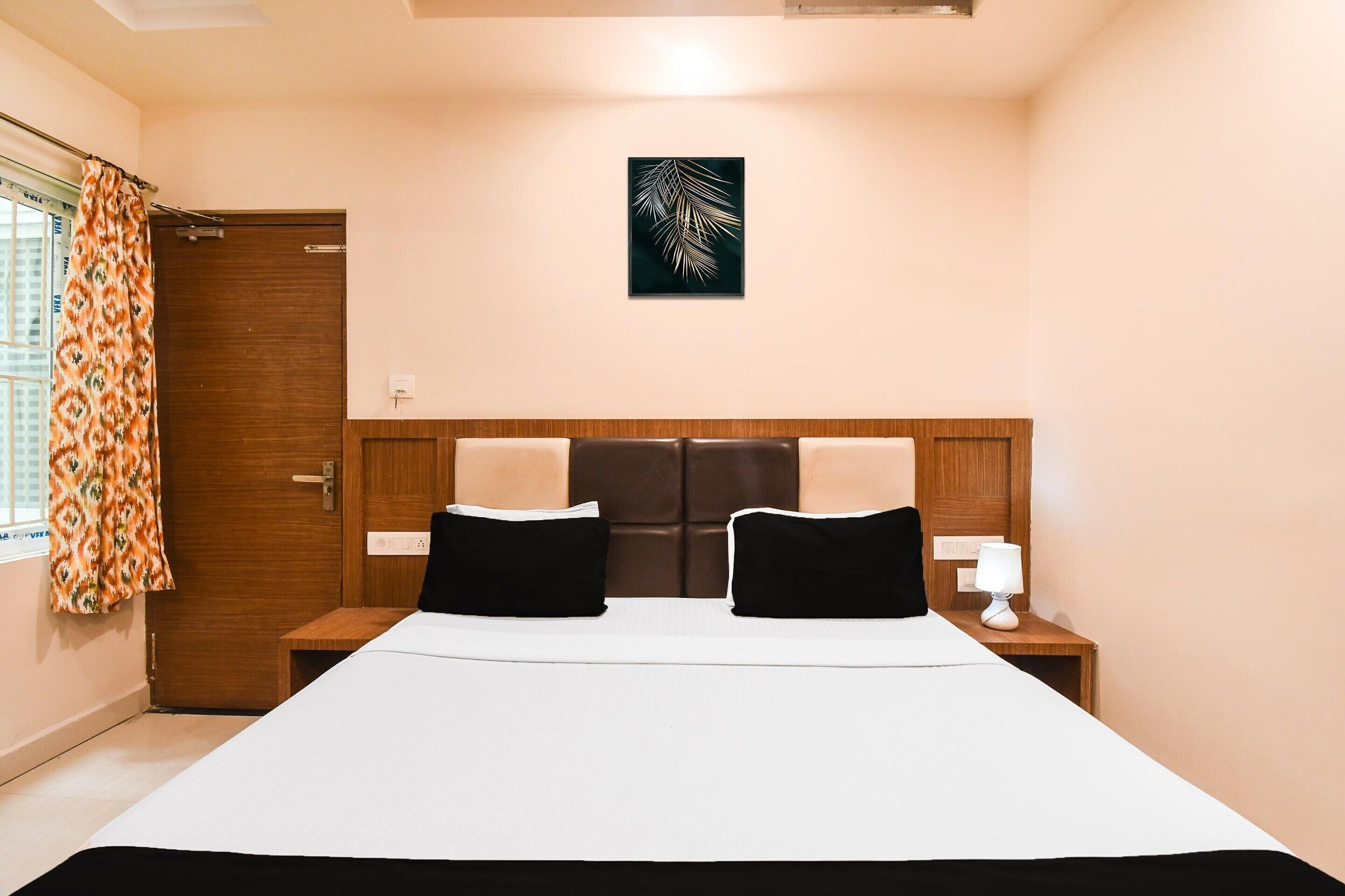 A hotel room with a bed, two bedside tables, a nightstand, a window with curtains, and a wall-mounted artwork.