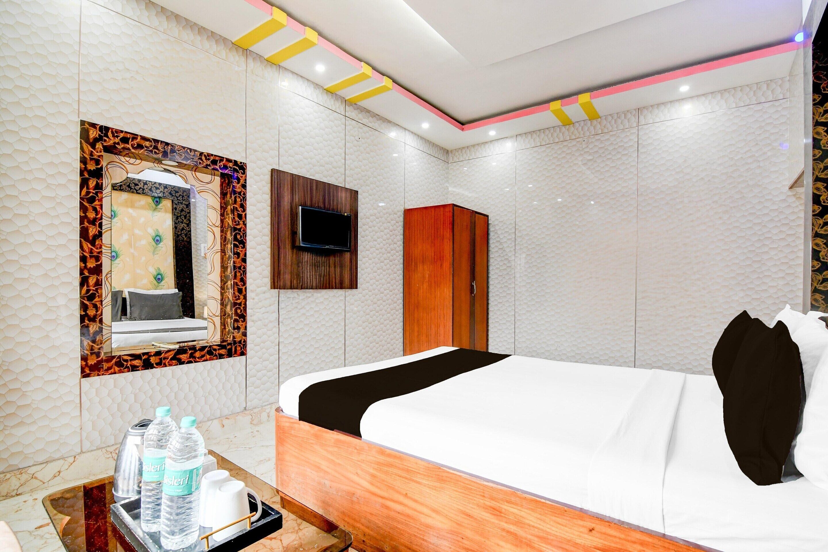 A hotel room with a bed, a TV, a wardrobe, and a mirror with a decorative frame.