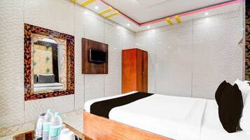 A hotel room with a bed, a TV, a wardrobe, and a mirror with a decorative frame.