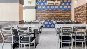 A dining area with multiple tables and chairs, a patterned wall, and a ceiling fan. - Premium Rupashi Guest House (Shrirampur)
