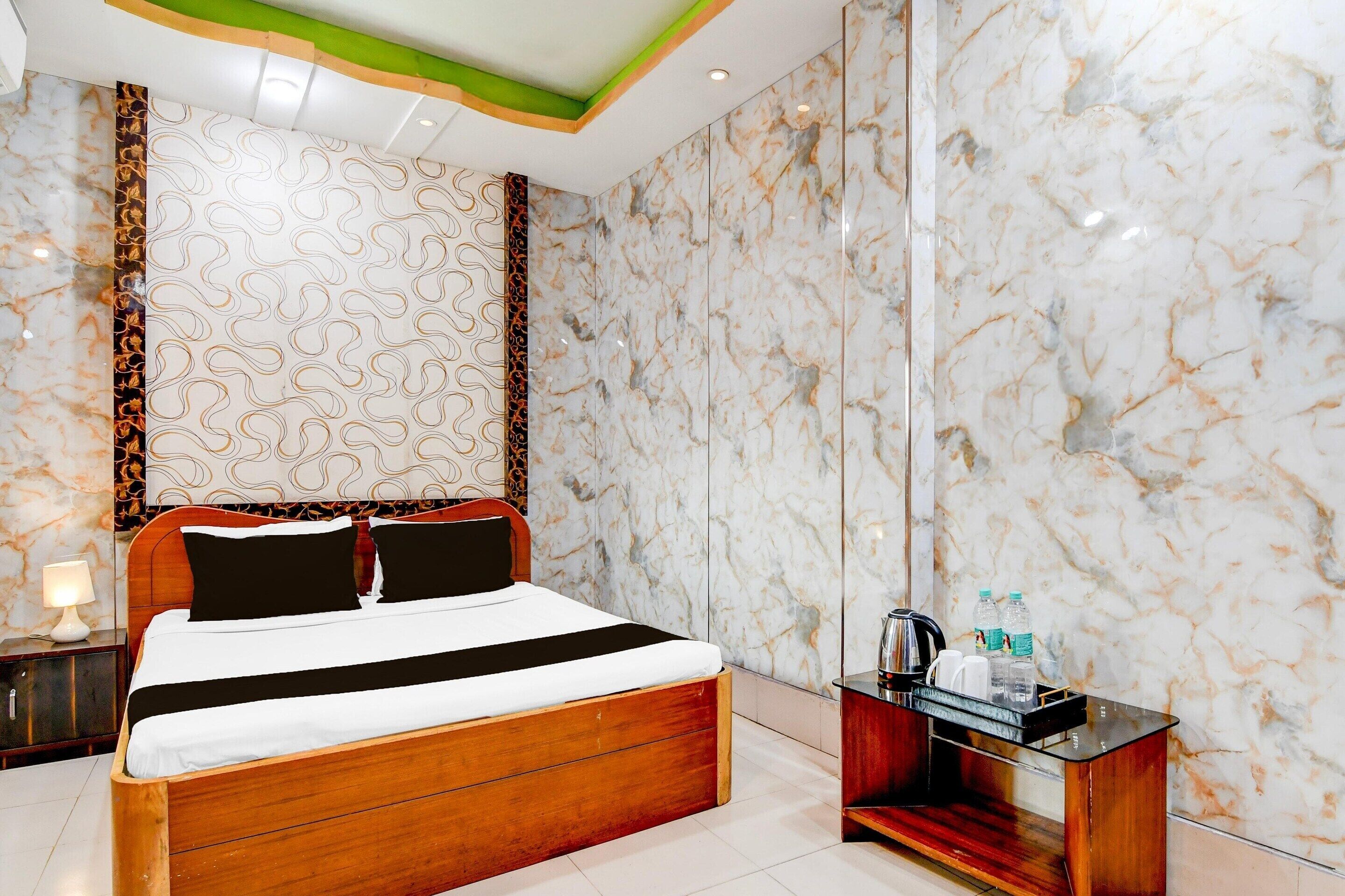 Quarto de hotel moderno com cama de madeira, paredes de mármore e uma pequena mesa de cabeceira com chaleira e garrafas.