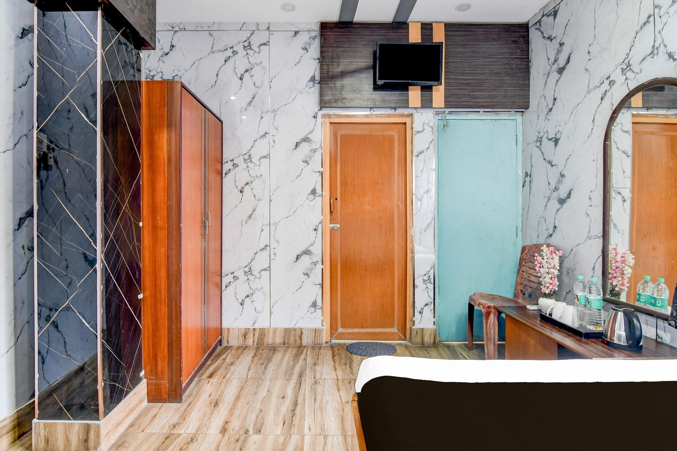 A hotel room with a wooden wardrobe, a television mounted on the wall, a wooden bench, and a bed.