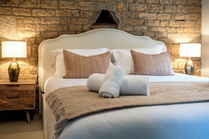 A neatly made bed with white and brown pillows, a rolled towel, and a wooden nightstand with a lamp. - The Potting Shed Banham Cottages (Bourton-on-the-Water)